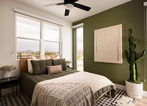 A bedroom with a bed, a cactus, and a fan.