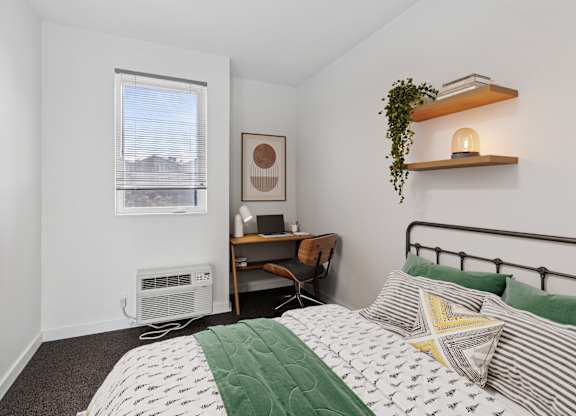 A bedroom with a bed, desk, and window.