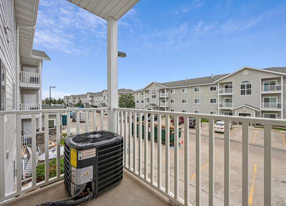 A balcony with a white railing and a black air conditioning unit on it.