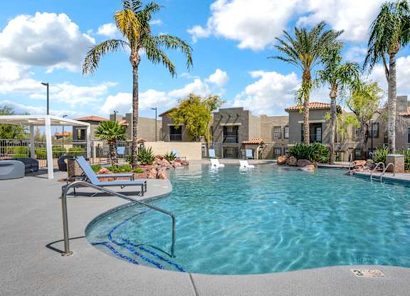 A pool surrounded by palm trees and a building in the background.