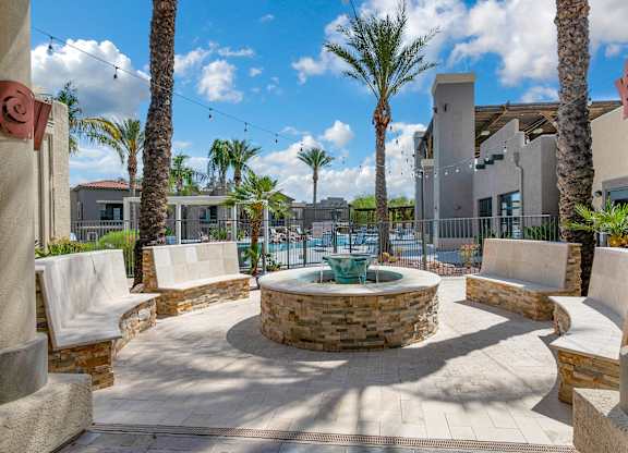 A courtyard with a fountain surrounded by palm trees and concrete pillars.