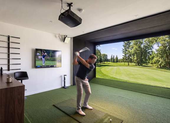 A man is playing golf in a room with a large screen showing a golf course.