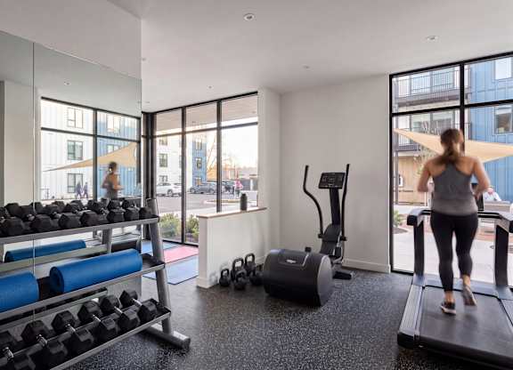 A woman is working out on a treadmill in a spacious gym with a view of the city.