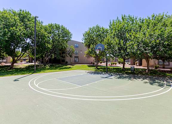 A basketball court surrounded by trees and a building in the background.