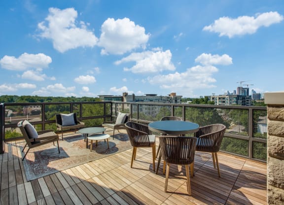 a patio with a round table and chairs on a wooden deck with a view of the city