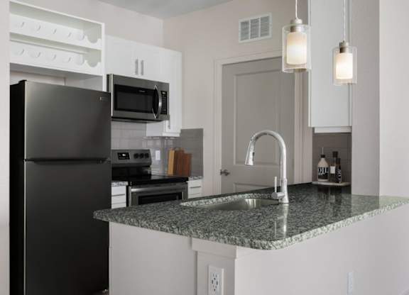 A kitchen with a black refrigerator and granite countertops.
