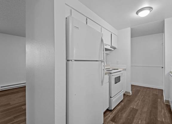 A white refrigerator in a kitchen with wood flooring.