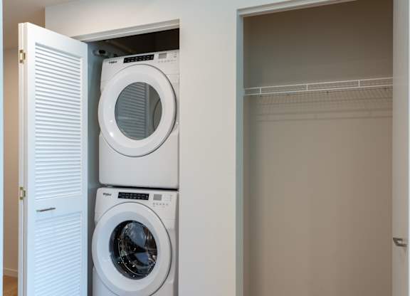 A white washing machine is in a cabinet under a white door.