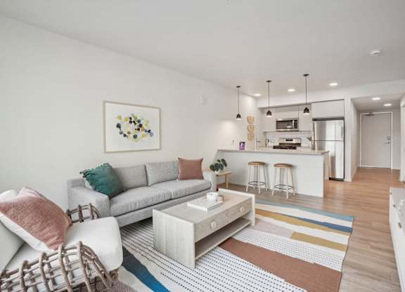 A modern living room with a grey sofa, a coffee table, and a bar area in the background.