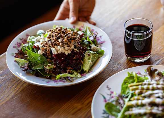 A person is sitting at a table with a plate of salad and a glass of red wine.