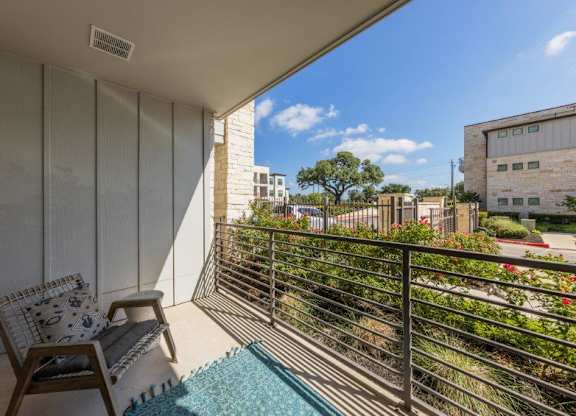 A balcony with a chair and a table with a cushion and a tablecloth on it.