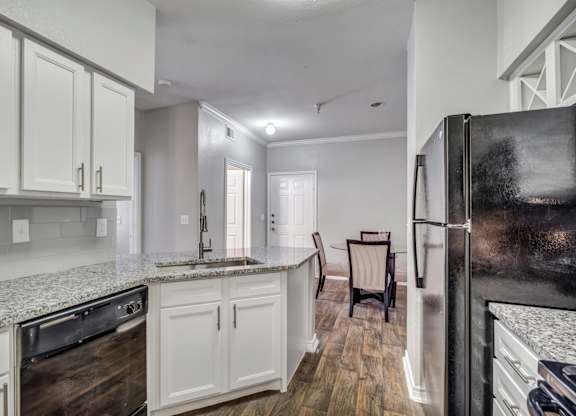 A kitchen with a black refrigerator, white cabinets, and a granite countertop.