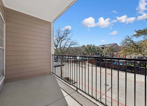 A balcony with a black railing and a view of a parking lot and trees.