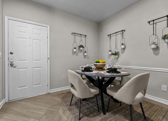 A dining room with a white door, a round table with four chairs, and three hanging planters.