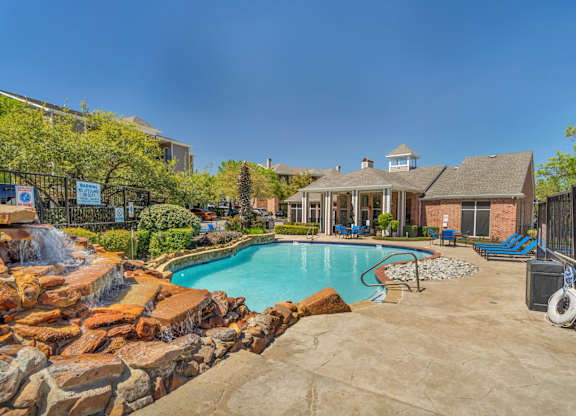 A large outdoor swimming pool surrounded by a stone wall and a fence.