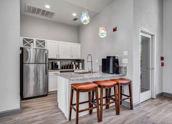 A kitchen with a refrigerator, bar stools, and pendant lights.