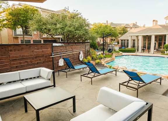 A poolside patio with a white couch and blue chairs.