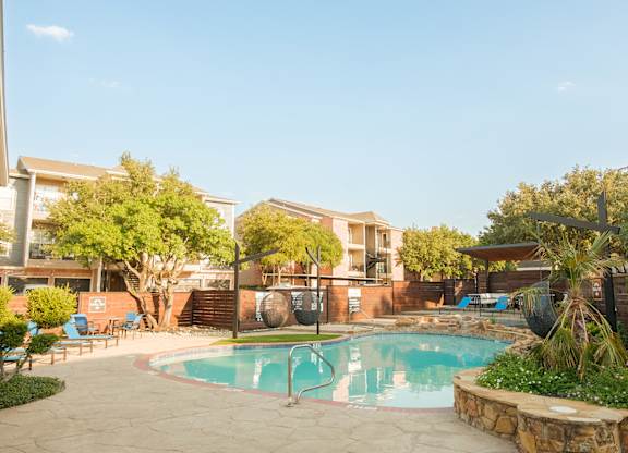 A swimming pool surrounded by a stone wall and trees.