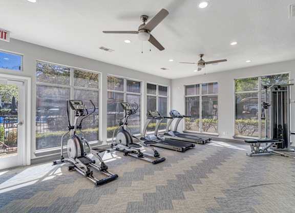 A gym with treadmills, exercise bikes, and a ceiling fan.
