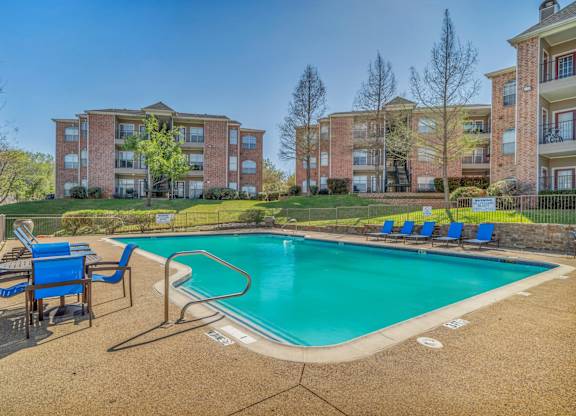 A swimming pool surrounded by blue chairs and apartment buildings in the background.