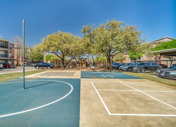 A tennis court is surrounded by trees and buildings.