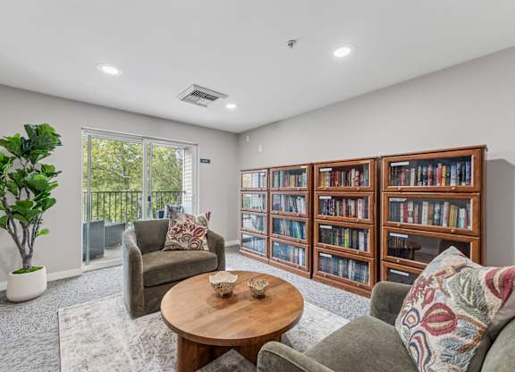 A living room with a grey couch, a wooden coffee table, a green plant, and a bookshelf filled with books.