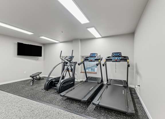 A gym with treadmills, elliptical machines, and a bench.