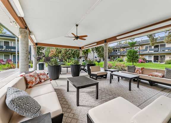 A patio with a white couch, black and white pillows, and a ceiling fan.
