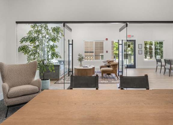 A room with a wooden table and chairs in the foreground and a glass wall in the background.