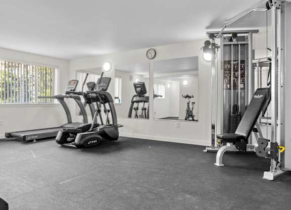 A gym with treadmills, weights, and a clock on the wall.