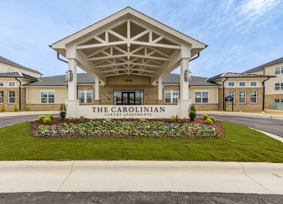 The Carolinian building has a white entrance canopy and a flower bed in front.