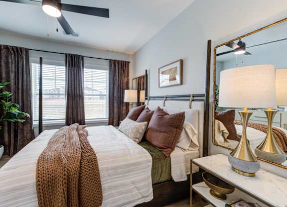 A bedroom with a large bed, a ceiling fan, and a mirror.