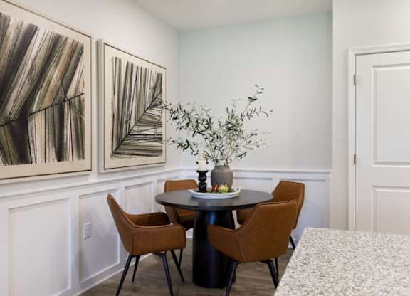 A dining room with a table, chairs, and two paintings on the wall.