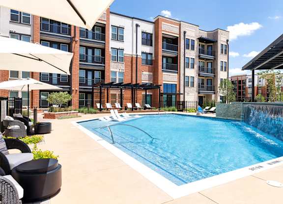 A pool surrounded by a patio with chairs and umbrellas.