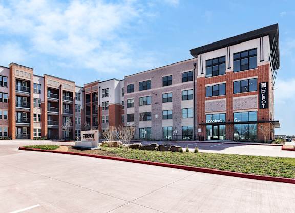 A row of modern apartment buildings with a parking lot in front.