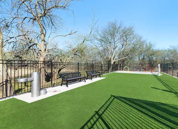 A park with a green field and a black fence.
