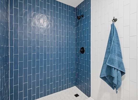 A blue tiled shower with a towel hanging on the wall.