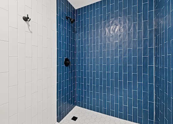 A blue tiled shower with a white tile floor.