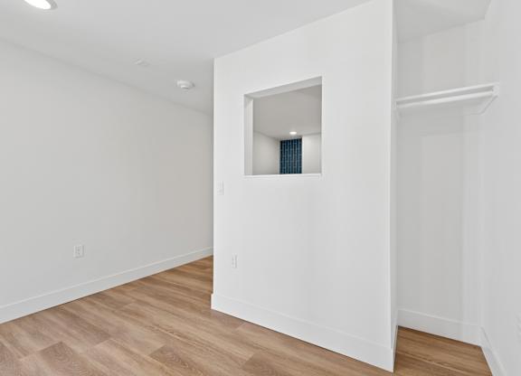 A white room with a small window and wooden flooring.