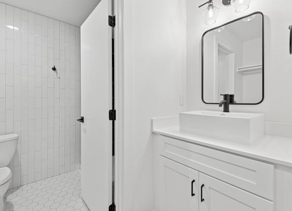 A white bathroom with a sink, mirror, and toilet.