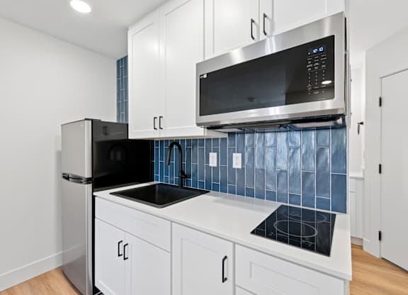 A kitchen with white cabinets and a black fridge.