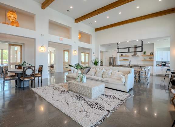 A spacious living room with a white sofa set and a rug in the center.
