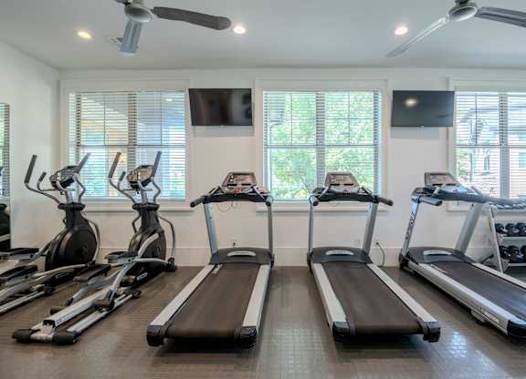 A gym with treadmills, elliptical machines, and a fan.