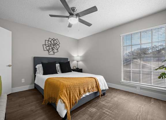 A bedroom with a bed, pillows, a ceiling fan, and a window with blinds.