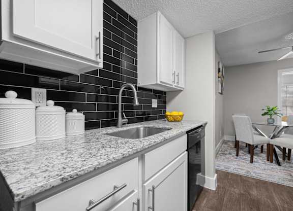 A kitchen with white cabinets and a black tile backsplash.
