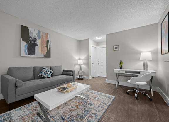 A living room with a grey couch, a white desk, and a painting on the wall.