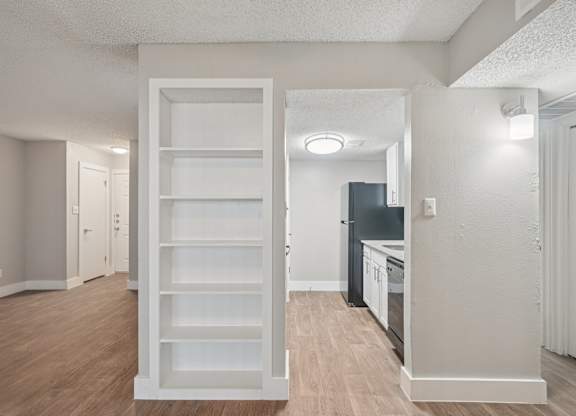 A white shelving unit in a room with a kitchen in the background.
