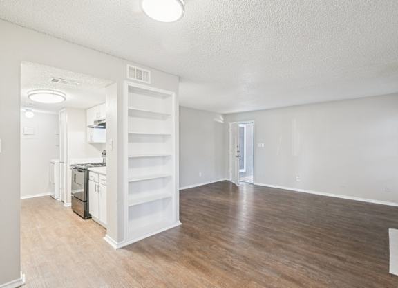 A white room with wood flooring and a kitchen area in the background.