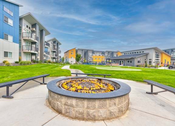 A fire pit with yellow leaves in the middle of a concrete patio.