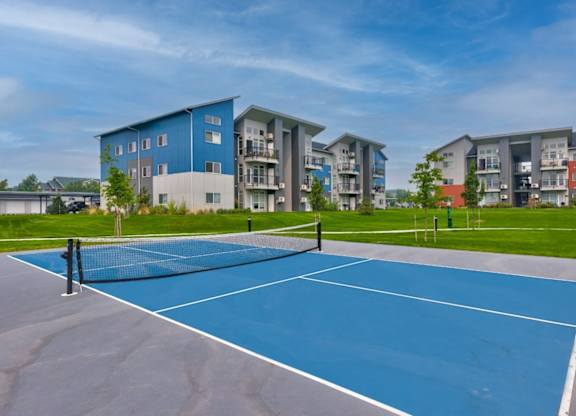 A tennis court is surrounded by apartment buildings.